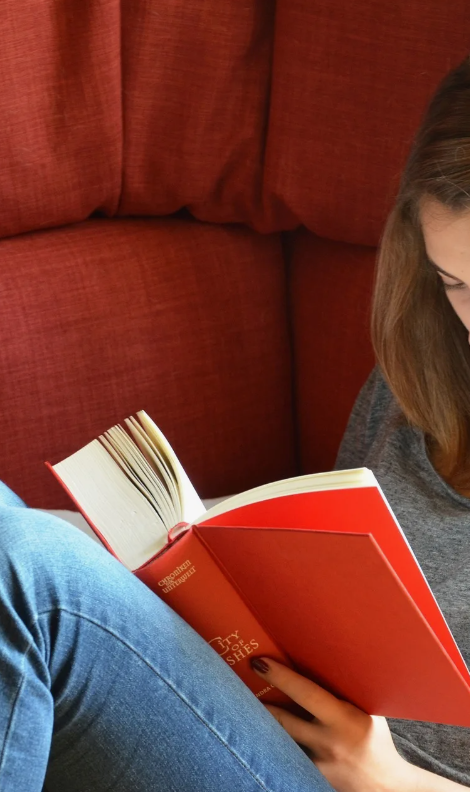 Женщина читает книгу на красном диване